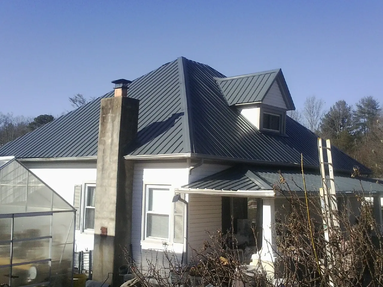 Dark blue standing seam metal roof on a white farmhouse with dormer — Slate & Tile Roof Repair by Roofing Brothers in Weston