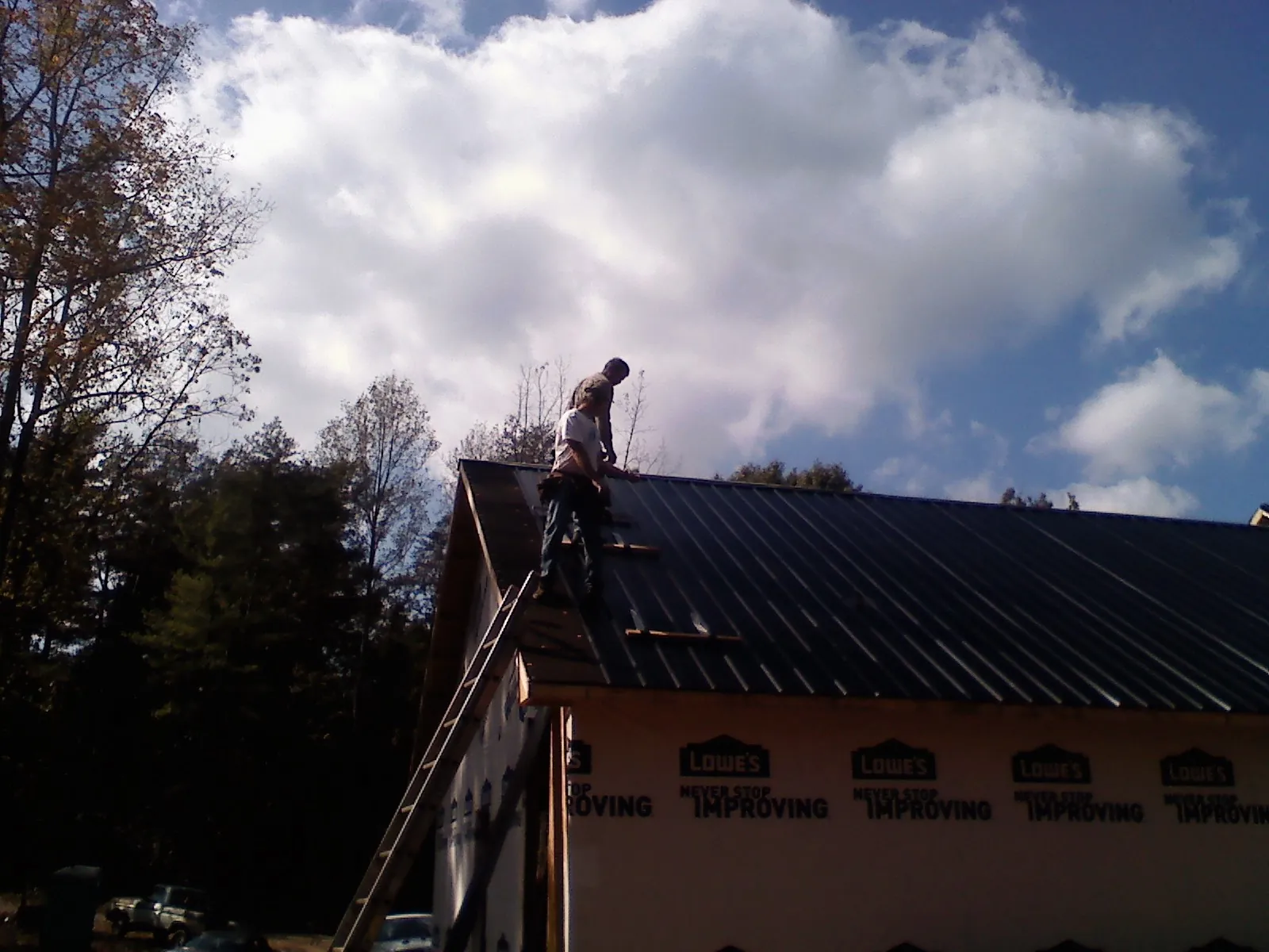 Roofer fastening dark metal panels high against a cloudy sky in Weston
